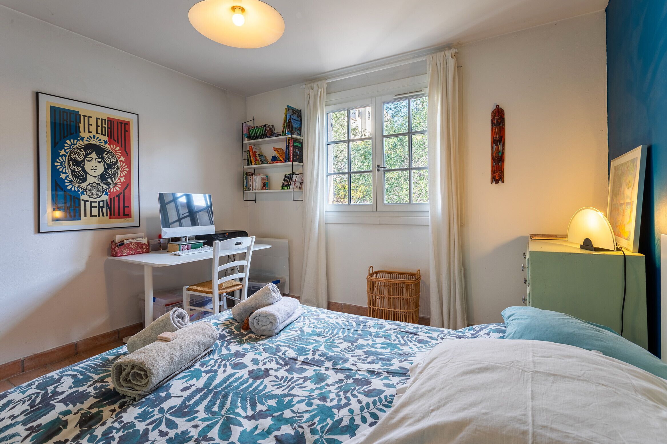 Une chambre à coucher comprenant un lit, un bureau, une chaise, une bibliothèque et une fenêtre avec des rideaux.