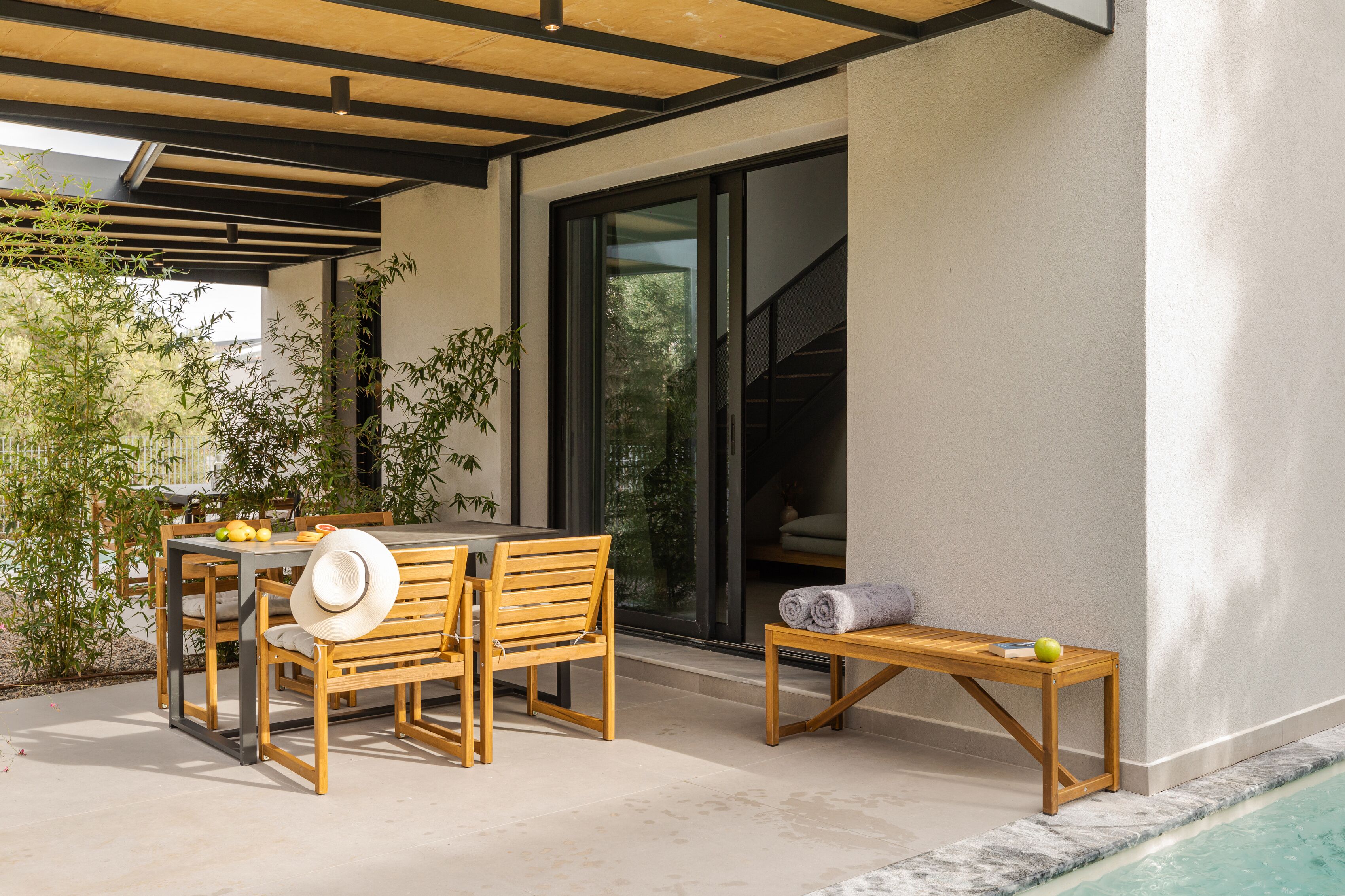 An outdoor patio with a wooden table and chairs, a small table with a towel and an apple, and a poolside area.