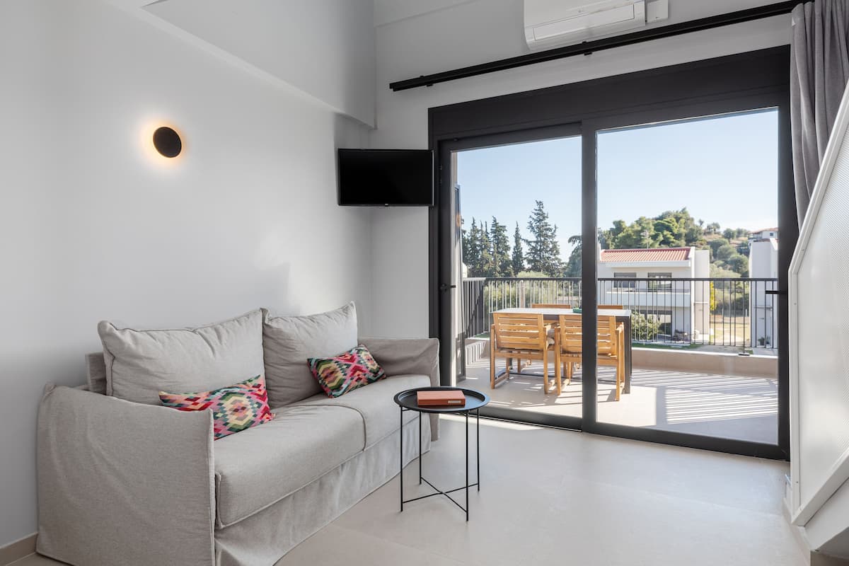 Ein modernes Wohnzimmer mit einer Couch, einem kleinen Tisch und Blick auf einen Balkon mit Gartenmöbeln.