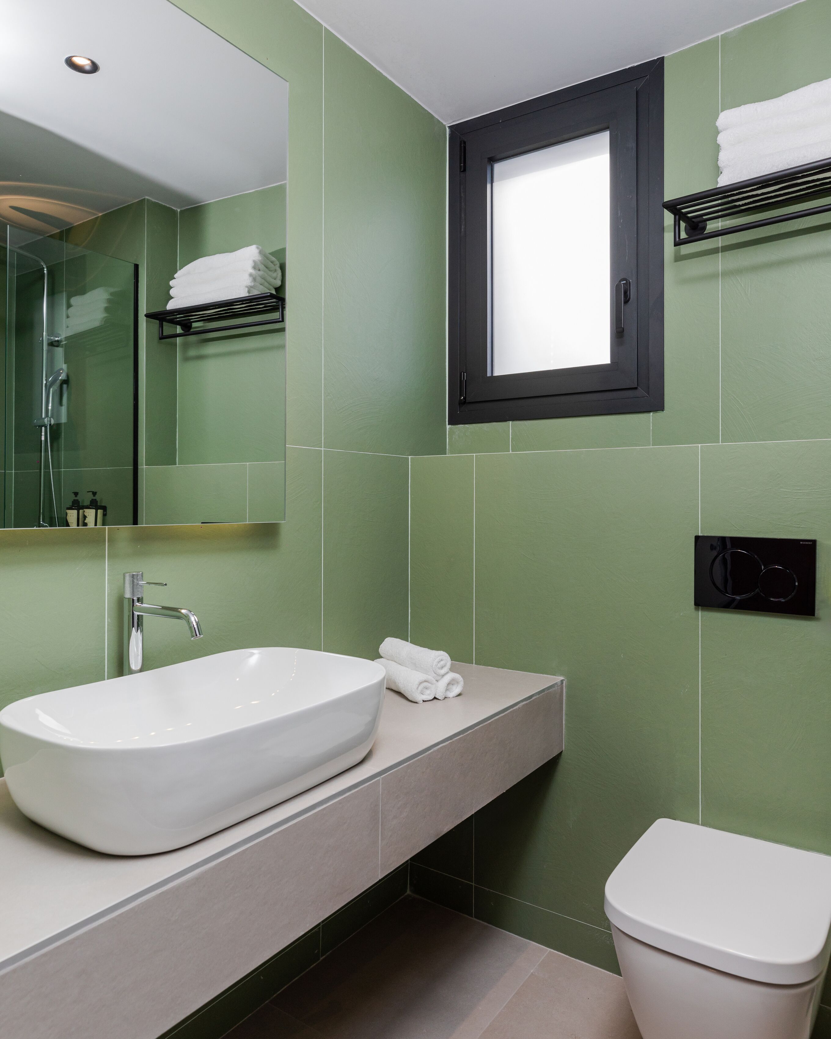 A modern bathroom with a large white sink, a mirror, a toilet, and a window.