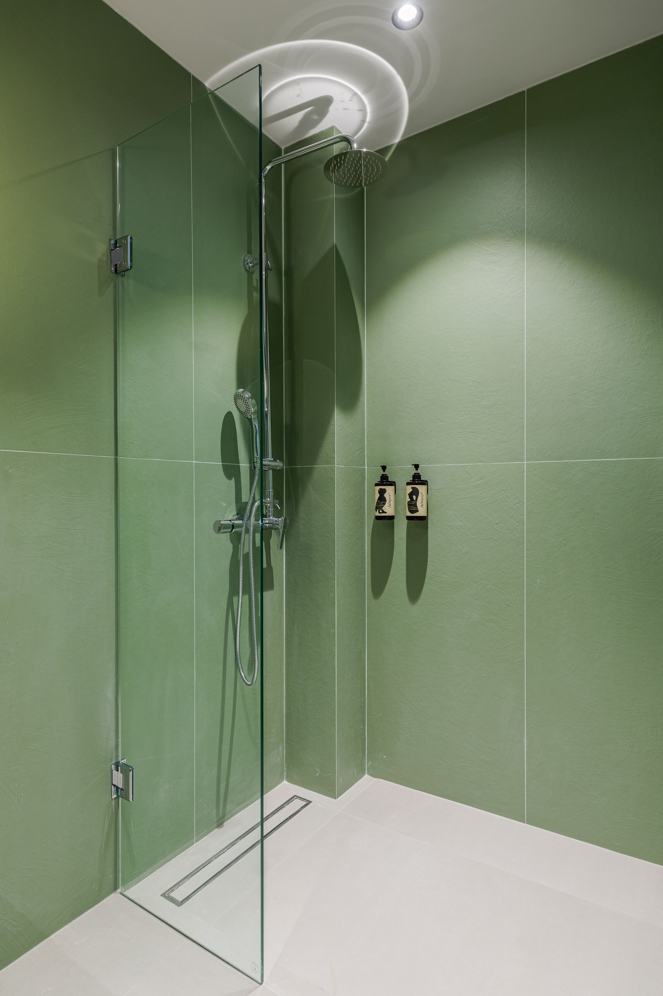 A glass-enclosed shower with a handheld showerhead and a wall-mounted faucet.
