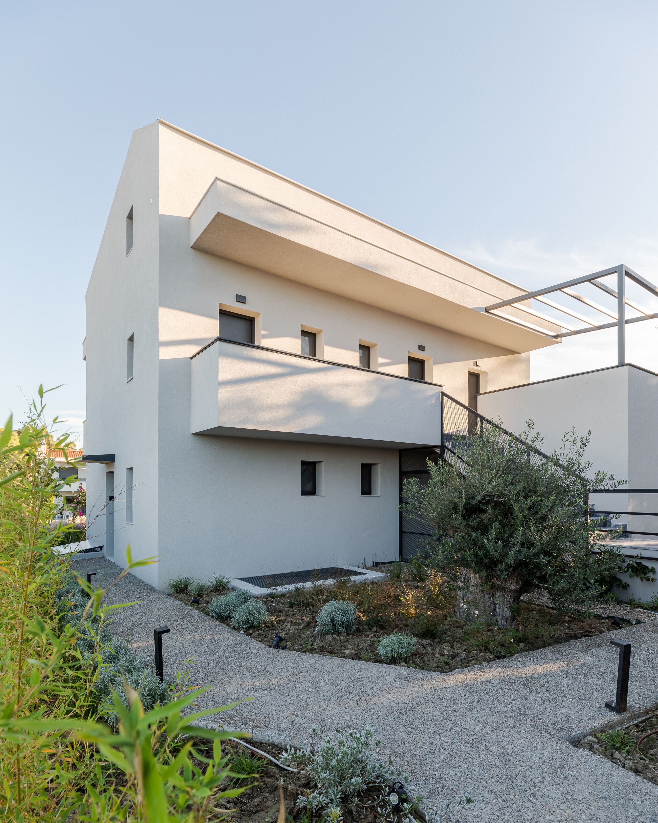 Un edificio moderno con techo plano, balcón y un pequeño jardín con grava y plantas.