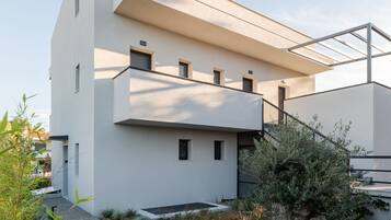 Un edificio moderno con techo plano, balcón y un pequeño jardín con grava y plantas.