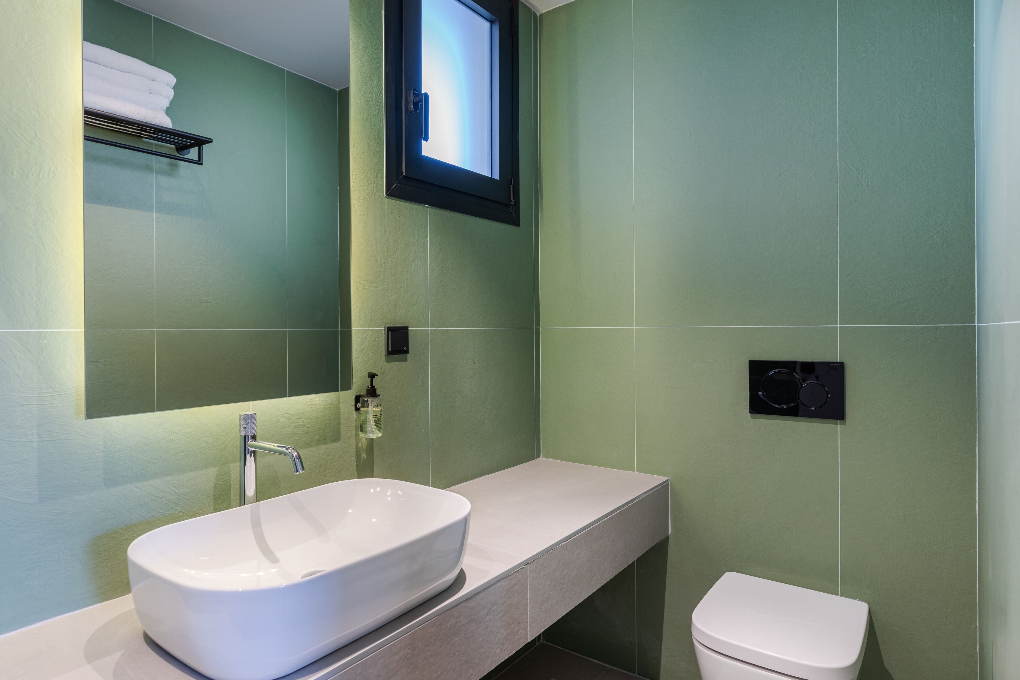 Un baño con lavamanos blanco, un espejo, una ventana y un inodoro.