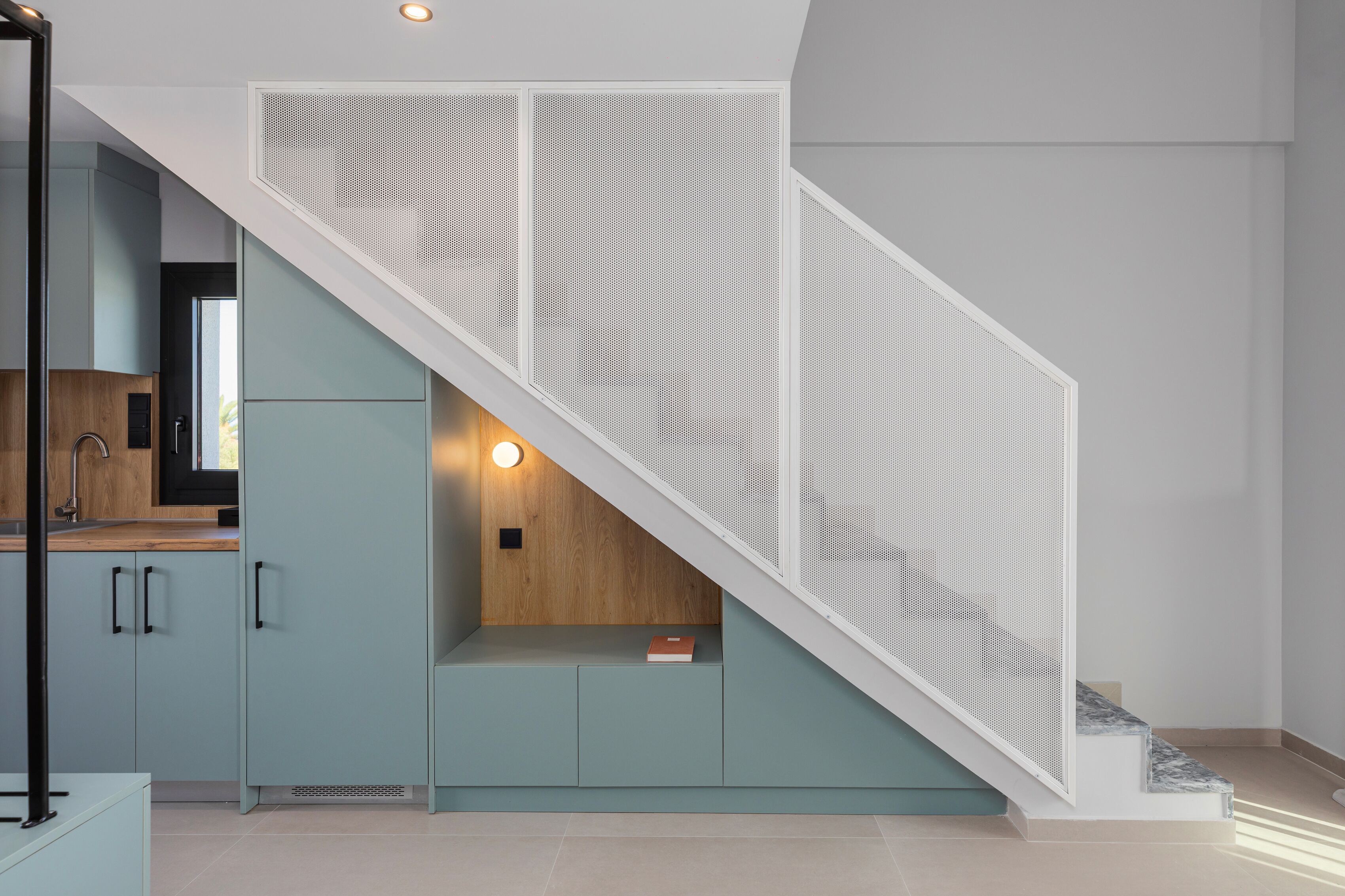 A modern kitchen with light blue cabinets, a wooden countertop, and a white staircase with a mesh railing.