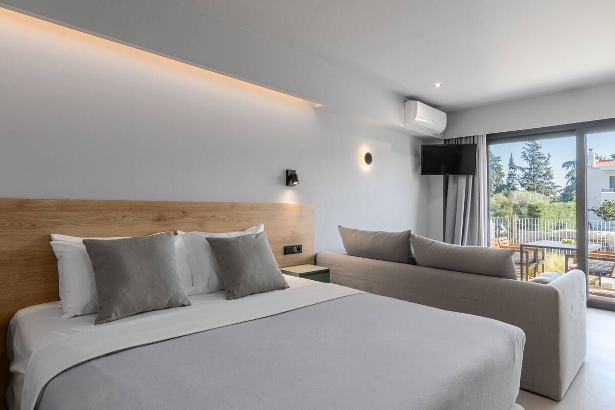 Ein modernes Hotelzimmer mit einem großen Bett, einer Couch, einem Flachbildfernseher und einem Balkon mit Blick ins Freie.