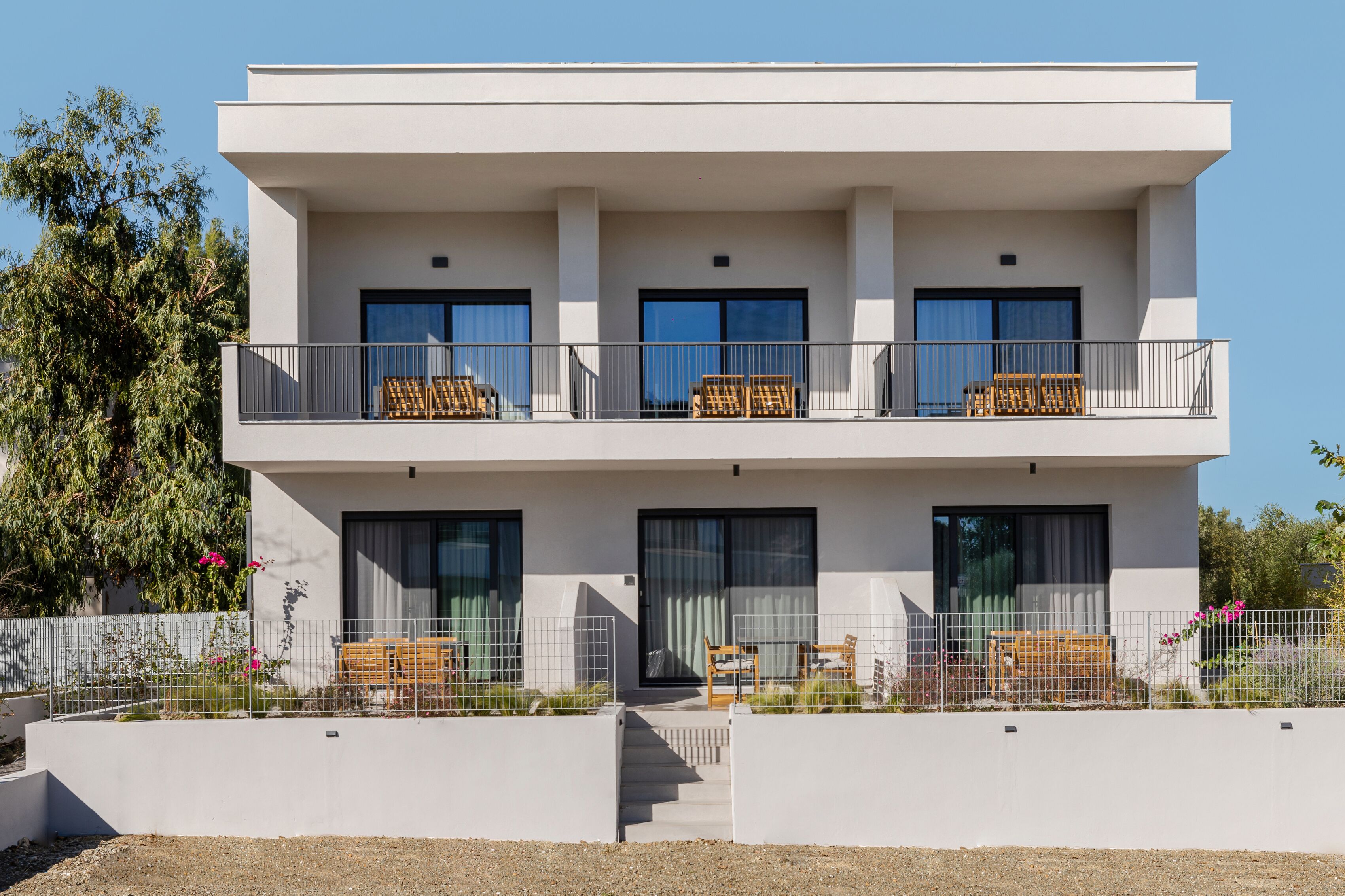 A modern two-story building with a balcony on the upper floor, featuring outdoor seating and a staircase leading to the entrance.