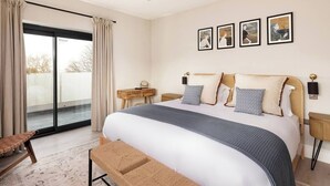 Une chambre moderne avec un grand lit, un banc, un bureau et une vue sur l’extérieur, accessible par une porte coulissante.