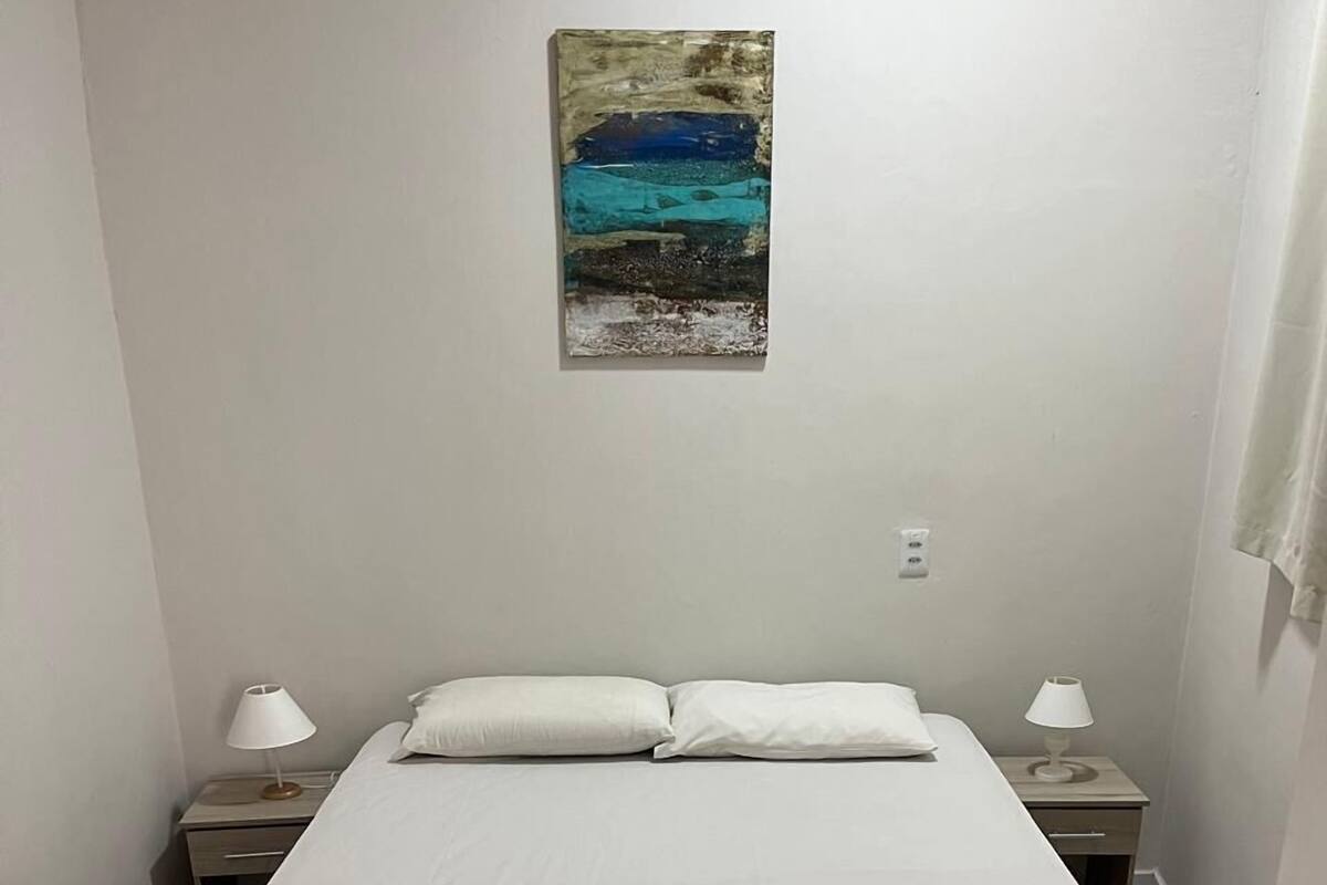 A single bed with a white mattress and a brown quilted bed skirt, flanked by two bedside tables with lamps, in a room with plain white walls and a tiled floor.
