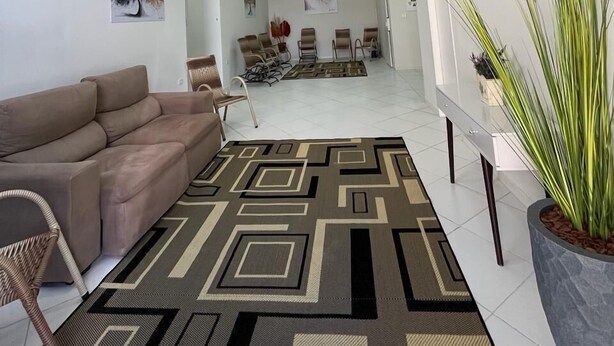 Ein modernes Wohnzimmer mit Sofa, Sesseln, einem gemusterten Teppich, einem Flachbildfernseher, Deckenventilatoren und Kunstwerken an den Wänden.