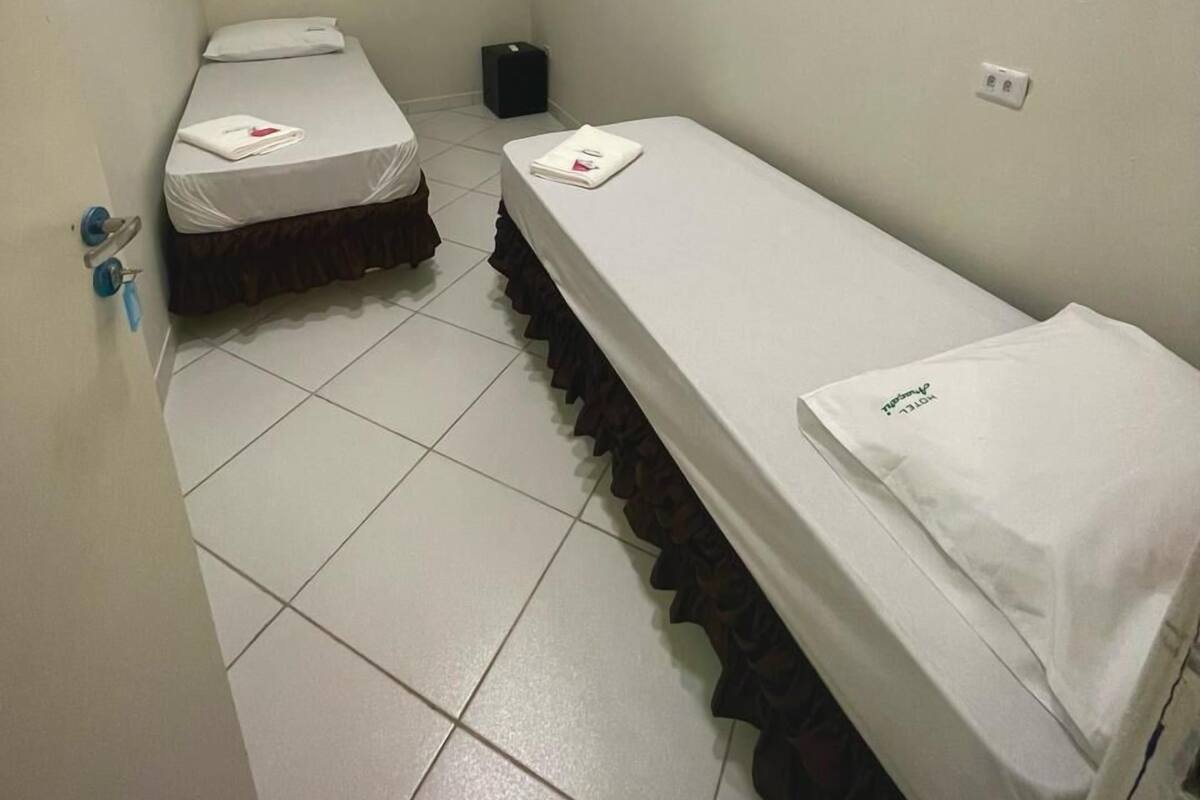 A small, narrow hotel room with two single beds, a white air conditioner, and a tiled floor.