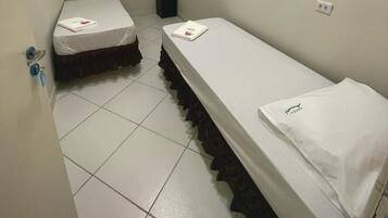 A small, narrow hotel room with two single beds, a white air conditioner, and a tiled floor.