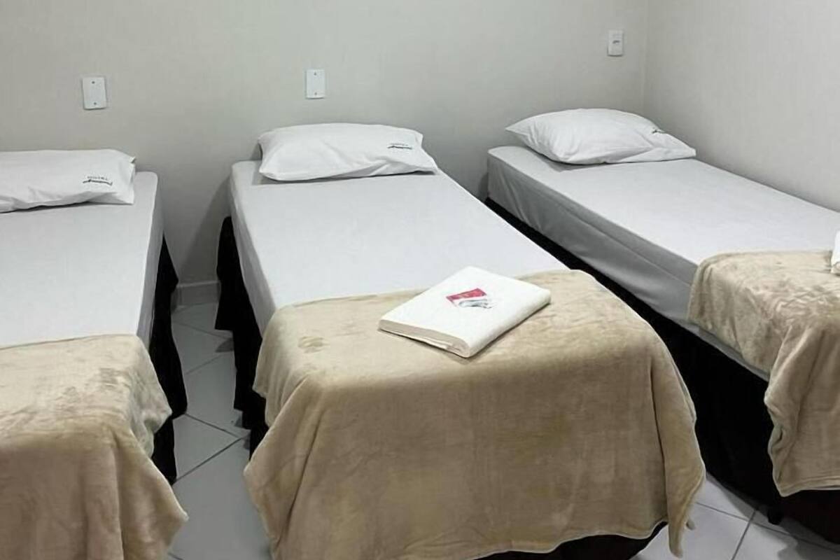 A room with three single beds, each with a white pillow and a beige blanket.
