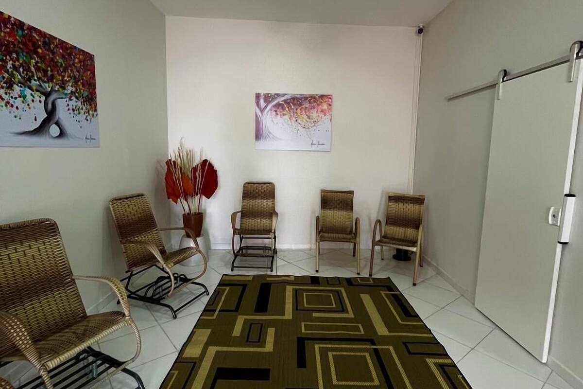 A room with a ceiling fan, four wicker chairs, a patterned rug, and two abstract paintings on the wall.