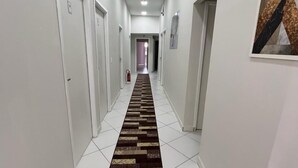 Ein langer, schmaler Korridor mit weißen Wänden, weiß gefliestem Boden und einem gemusterten Teppich.