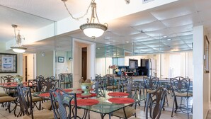 A spacious dining area with glass tables and chairs, a chandelier, and a kitchen in the background.
