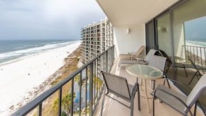 A balcony with a glass table and chairs overlooking a beach and ocean.