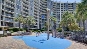 A hotel courtyard with a blue play area, palm trees, and a multi-story building in the background.