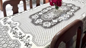 A dining area with a table set for four, a vase with flowers, and a view into a kitchen with wooden cabinets and a microwave. - Anastera Home Vila (Kigali)