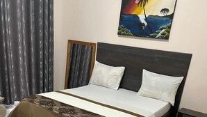 A neatly made bed with a white and brown bedspread, a dark headboard, and a painting of a tropical scene above it. - Anastera Home Vila (Kigali)