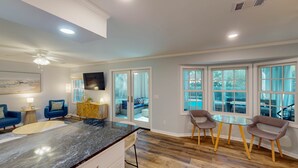 A modern kitchen with a granite countertop, wooden cabinets, and a dining area with glass tables and chairs. - A Lifelong Dream - 3 bedroom, 2 bath with private swimming pool (Jekyll Island)