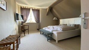 Ein Schlafzimmer mit Bett, Schreibtisch, Stuhl, Fernseher und einem Fenster mit Vorhängen.