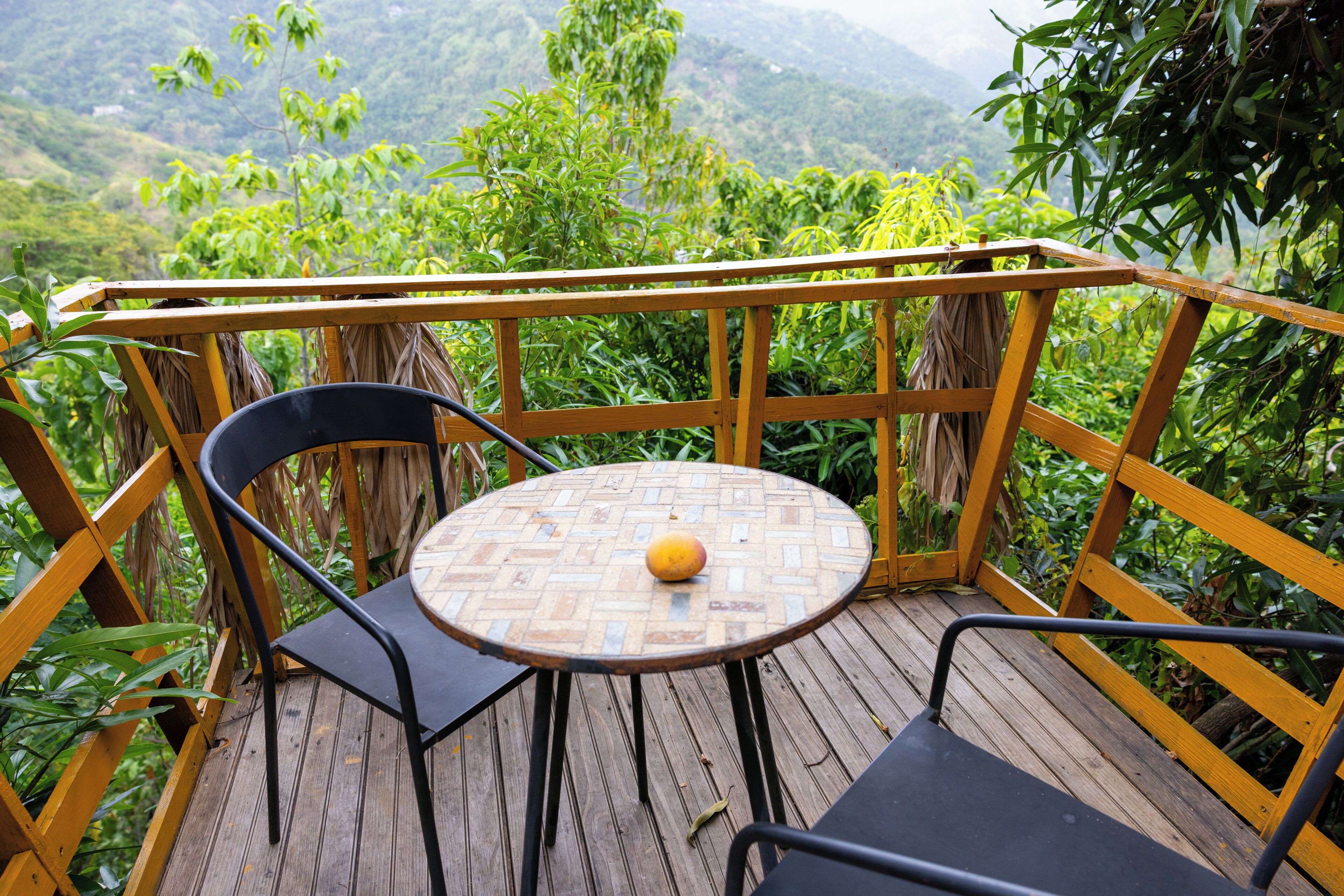 A wooden deck with a round table and two chairs, overlooking a lush green landscape.