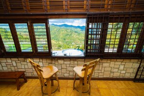 Una habitación con pared de piedra, dos sillas de madera y vistas a un paisaje montañoso a través de amplios ventanales.