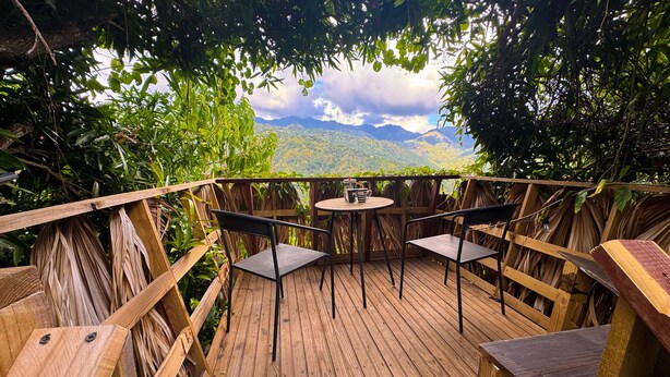 A wooden deck with a table and chairs, surrounded by lush greenery and a view of distant mountains. - Reggae Legends Estate (Kingston)