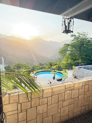 A swimming pool with a view of mountains, a stone wall, and a hanging light fixture. - Reggae Legends Estate (Kingston)