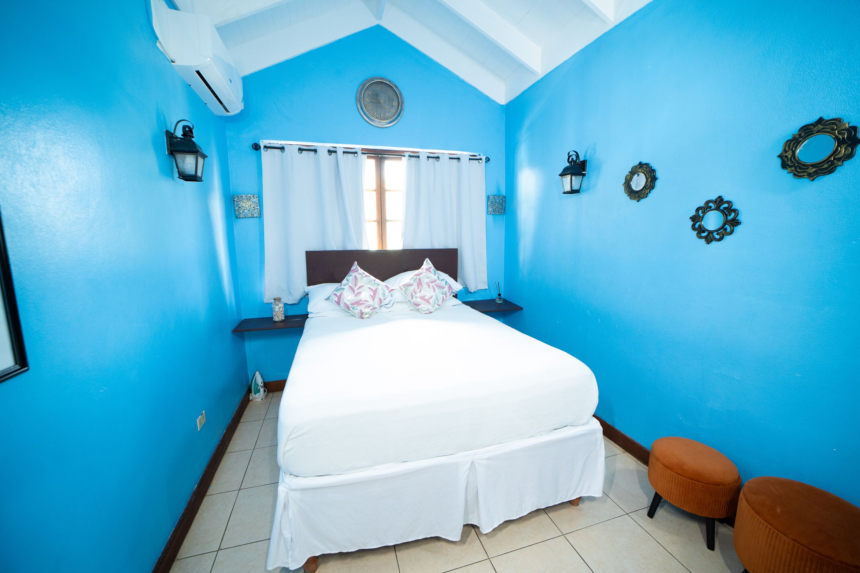 Un dormitorio con una cama grande, una mesita de noche, un reloj de pared y una ventana con cortinas.