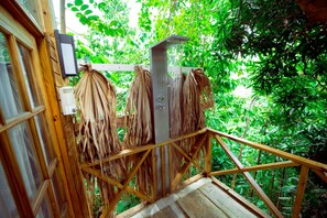 Uma escadaria de madeira leva a uma área de chuveiro com um chuveiro de efeito chuva em metal, tudo envolto por vegetação verde exuberante.