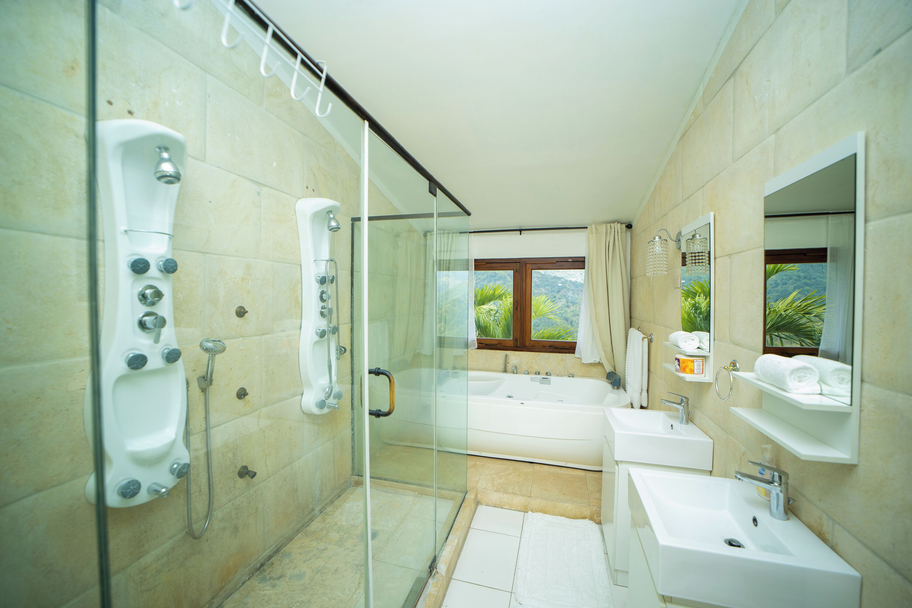 Une salle de bain moderne dotée d’une douche à parois de verre, d’une baignoire, de deux lavabos et d’un grand miroir.
