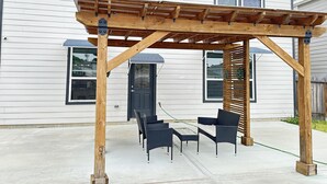 Een houten pergola met een tafel en stoelen voor een huis.