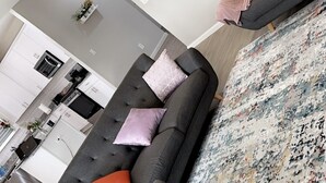 Een moderne woonkamer met een grijze bank, een bijpassende fauteuil en een kamerkleed met dessin.