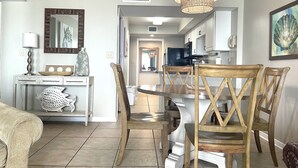 A dining area with a round table, wooden chairs, and a hanging light fixture. - Surf Side Shores 1206  New Sofa   3 bd / 3 bth gulf-front corner unit (Gulf Shores)