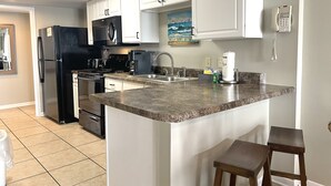 A modern kitchen with white cabinets, a black refrigerator, a microwave, a stove, and a coffee maker. There is a painting on the wall and a phone on the wall. - Surf Side Shores 1206  New Sofa   3 bd / 3 bth gulf-front corner unit (Gulf Shores)
