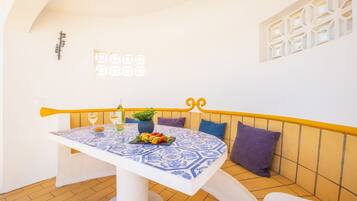 Un comedor con una mesa dispuesta para dos personas, un banco con cojines y una pared decorativa con un diseño geométrico.