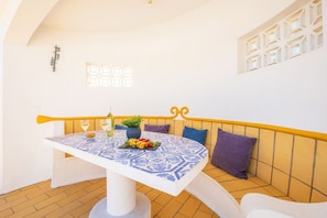 Un comedor con una mesa dispuesta para dos personas, un banco con cojines y una pared decorativa con un diseño geométrico.
