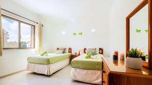 A hotel room with two single beds, a wooden dresser, a mirror, and a window with curtains. - Villa Renaissance (Lagoa)