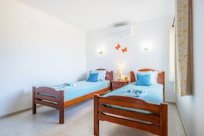 Una habitación con dos camas de madera, aire acondicionado instalado en la pared y una mesita de noche con lámpara.