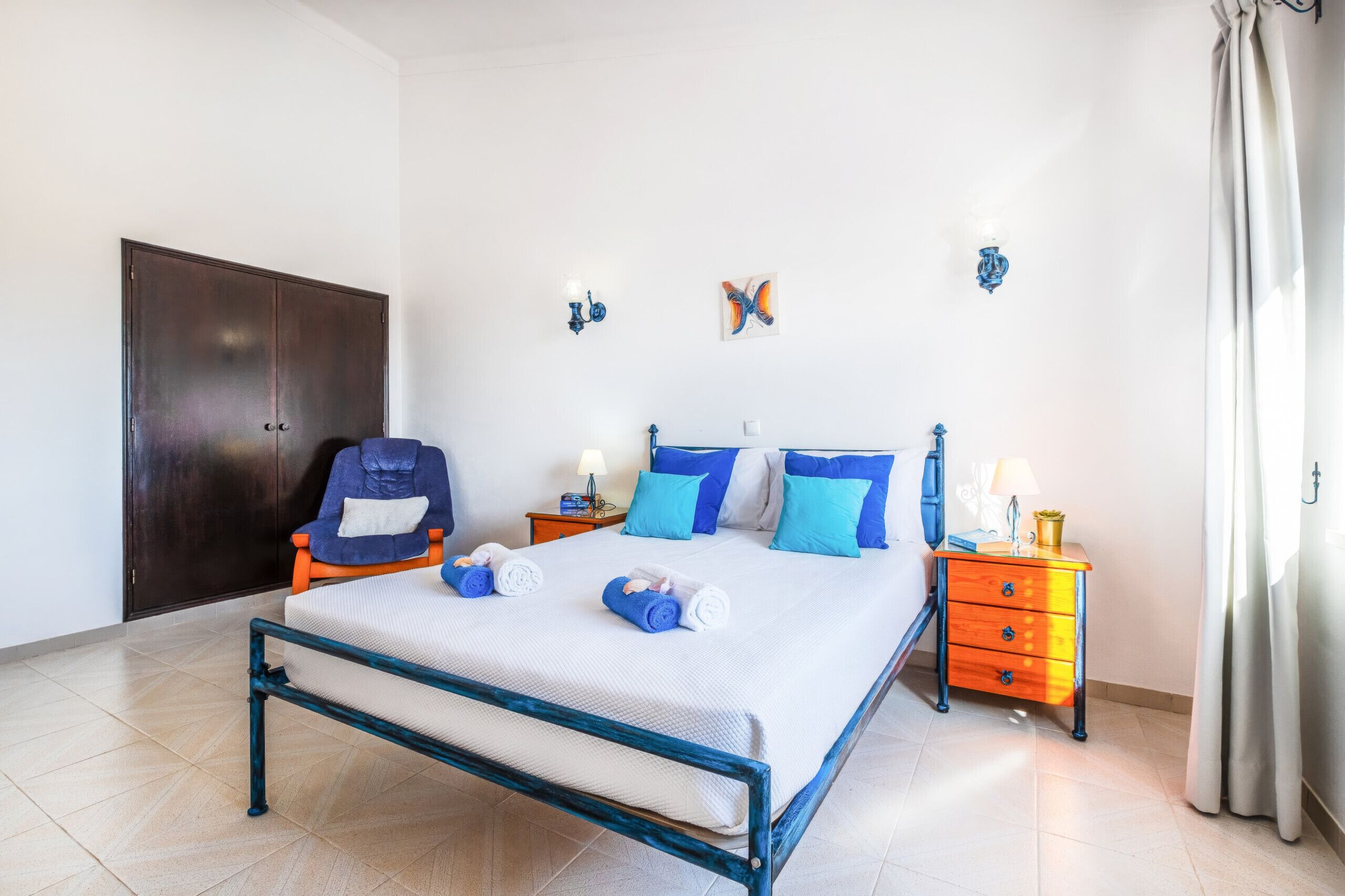 A hotel room with a bed, a chair, a nightstand, and a wardrobe.