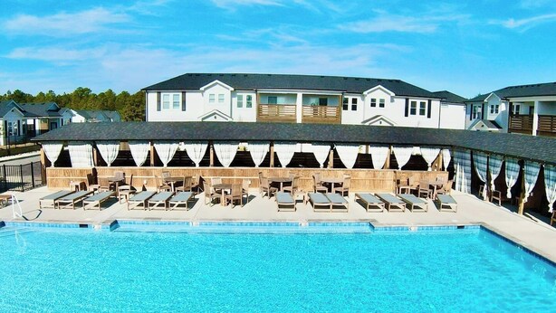 Ein Swimmingpool mit Liegestühlen und einer überdachten Sitzgelegenheit, umgeben von einem Gebäude mit flachem Dach und zahlreichen Fenstern.