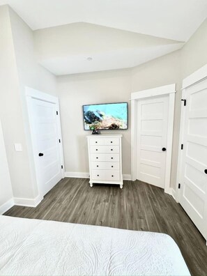A bedroom with a bed, a dresser, a television, and white doors.