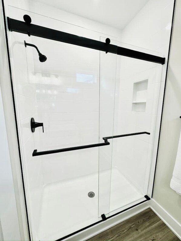 A glass-enclosed shower with a black handle and a black towel rack.