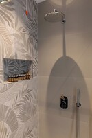Un espacio de ducha con cabezal de ducha tipo lluvia, un cabezal de ducha de mano y un estante con botellas.
