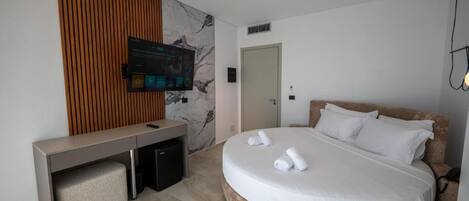 A modern hotel room with a round bed, a desk with a computer, a flat-screen TV mounted on the wall, and a wooden panel design on the wall.