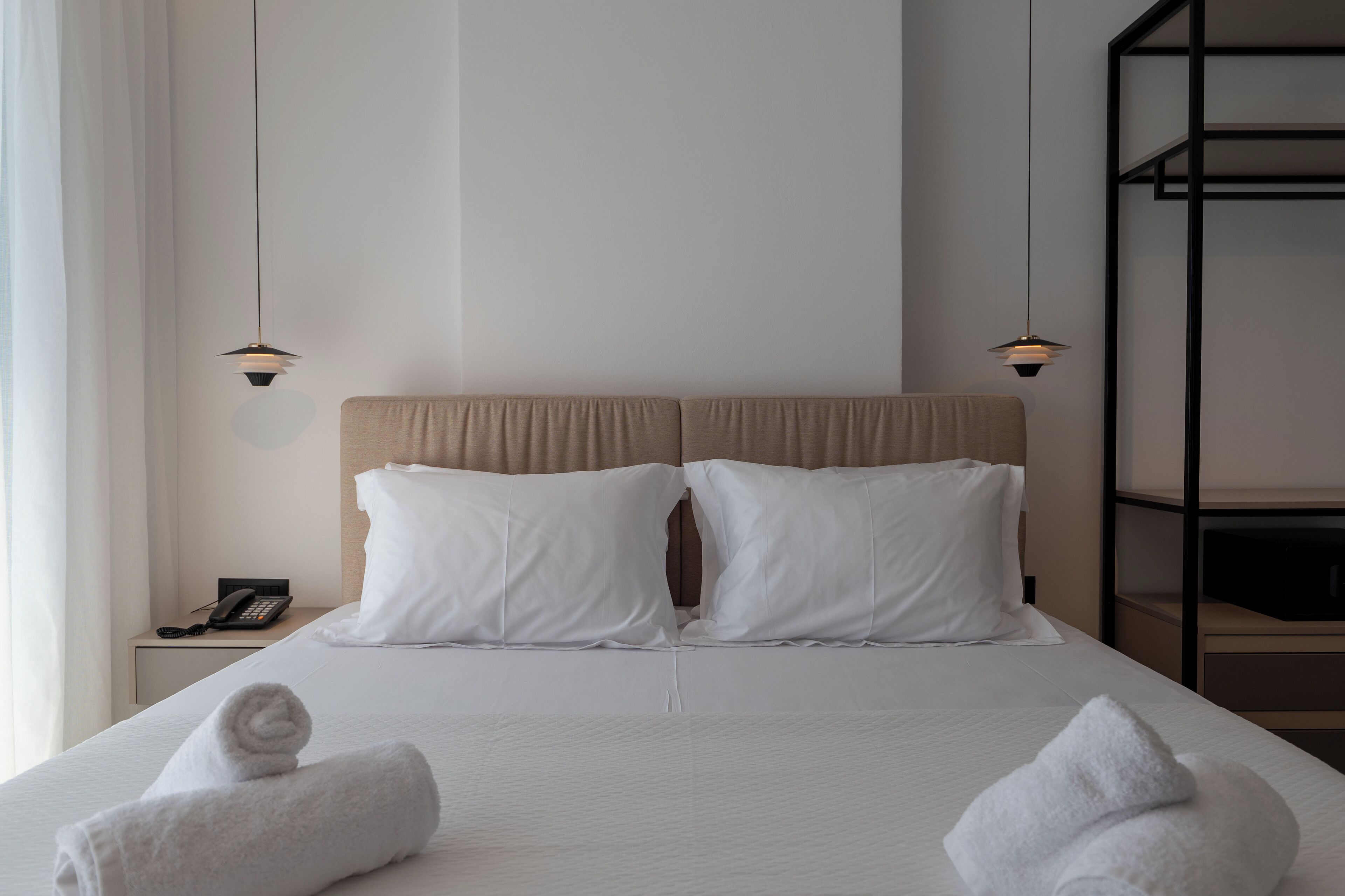 A neatly made bed with white linens and two rolled towels at the foot of the bed.