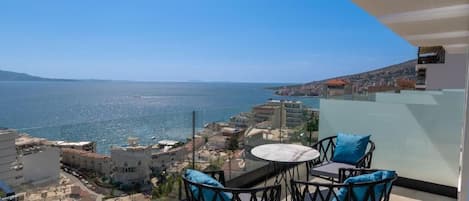 A balcony with a table and chairs overlooking a coastal cityscape.