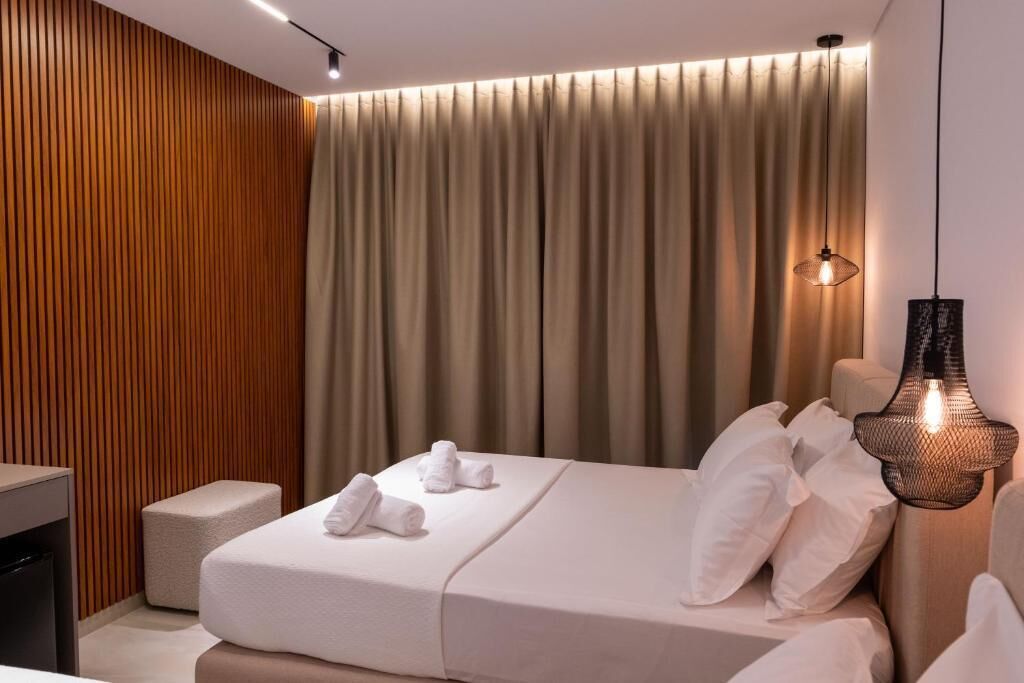 Una habitación de hotel moderna con una cama bien hecha, una mesita de noche pequeña y una lámpara colgante.